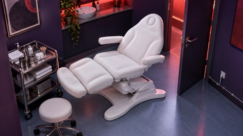 White swivel treatment chair positioned too close to a trolley, stool and doorway in a compact purple treatment room